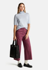 Jasnoniebieski golf z krótkim rękawem, wysokie bordowe spodnie szerokie w nogawkach, czarna torba na ramię z złotymi detalami, białe skarpetki, czarne mokasyny.