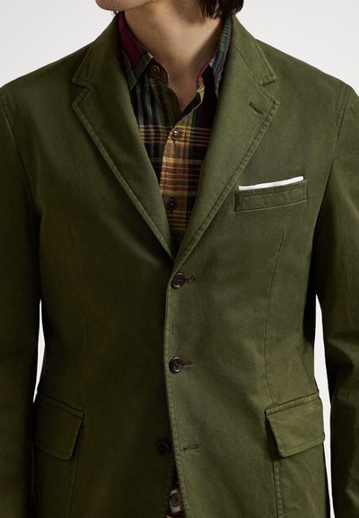 Βαμβακερό σακάκι χακί με εφαρμοστή γραμμή, δύο μπροστινές τσέπες, τρία κουμπιά και ένα λευκό μαντηλάκι στην τσέπη στο στήθος.