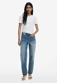 Weißes Baumwoll-T-Shirt mit kurzen Ärmeln und kleinem Logo, kombiniert mit blauen Jeans im lässigen Schnitt mit kontrastierenden Nähten.