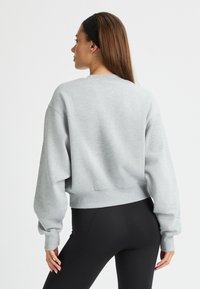Sudadera gris recortada con mangas largas abullonadas y cuello redondo, hecha de una tela suave. Combinada con leggings negros ajustados.