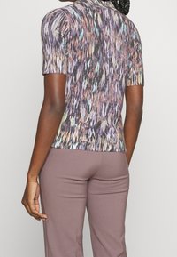 Kortærmet sweater, rillet tekstur, multicolor mønster med lilla, grønne og blå nuancer. Tætsiddende design, moderat halsudskæring og blødt stof.