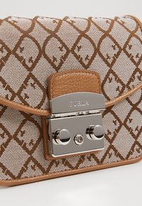 Brązowa torebka z materiału w wzory, z paskiem ze skóry, wyposażona w srebrną klamrę z dwoma okrągłymi przyciskami oraz logo na przodzie.