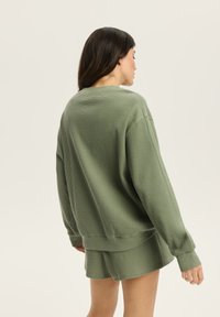 Zielony sweatshirt z dzianiny waffle, z długimi rękawami i ściągaczami, o luźnym kroju i wysokim okrągłym dekolcie.