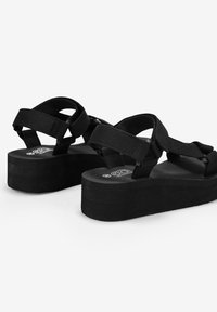 Sandali platform neri con ampie cinghie in tessuto e suola a trama, dotati di un design della suola a doppio strato per maggiore altezza e stabilità.
