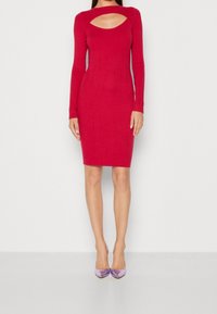 Robe en tricot rouge à côtes avec des manches longues et un décolleté découpé. Texture à motifs et design ajusté. Associée à des talons brillants violets.