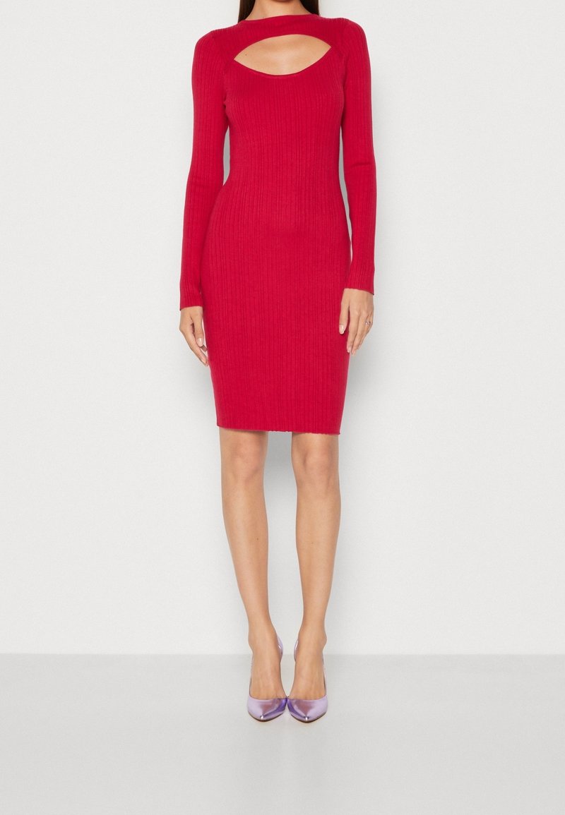 Robe en tricot rouge à côtes avec des manches longues et un décolleté découpé. Texture à motifs et design ajusté. Associée à des talons brillants violets.