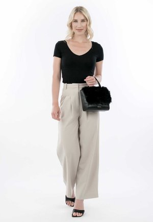 Top nero attillato, pantaloni beige a vita alta, tacchi neri open-toe, con una piccola borsa nera con un accento in pelliccia. Sfondo bianco semplice.
