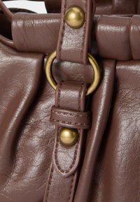 Brown leather handbag features a fold-over design with a gold-tone metal ring and snap button, highlighting stitched details and a textured finish.