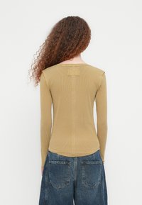 Μπλούζα με μακριά μανίκια και ριπ ύφανση σε μουσταρδί κίτρινο, με στρογγυλή λαιμόκοψη, που διαθέτει τετράγωνη λεπτομέρεια στην άνω πλάτη και εφαρμοστά μανίκια.