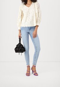 Vit spetsblus med puffärmar, ljusblå skinny jeans, svart mönstrad handväska och lila remsandaler. Släta ytor och kontrasterande färger.