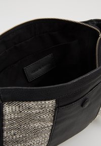 Pochette intrecciata in bianco e nero con bordi in pelle nera, zipper aperta e etichetta "mint & berry" visibile all'interno.