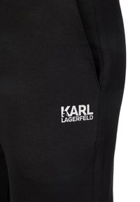 Pantalones deportivos negros de algodón, con superficie texturizada, bolsillos laterales y un logo "KARL LAGERFELD" bordado en blanco.