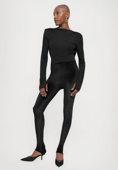Black long-sleeve top paired with high-waisted, textured black leggings. The outfit features a fitted design and is complemented by pointed black heels.