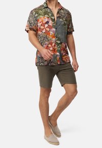 Short-sleeve, multi-colored shirt with geometric and floral patterns, paired with olive green shorts and beige slip-on shoes.