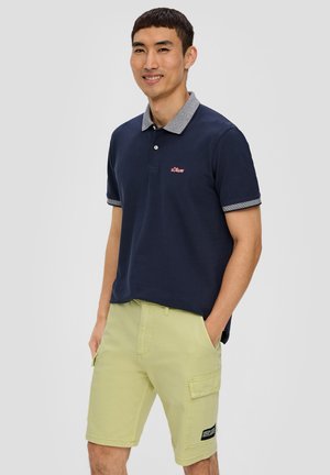 Mornarska polo majica sivi ovratnik, s malim crvenim logom, uparen s svijetlozelenim cargo kratkim hlačama s džepovima i crnom etiketom.