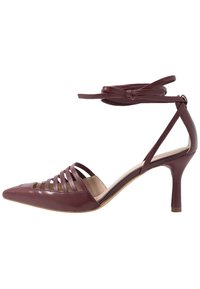 Scarpa col tacco alta color bordeaux con punta affusolata, cinturini con tagli e lacci alla caviglia. Texture in pelle liscia e design del tacco sottile.