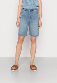 Ljusblå denim-Bermudashorts med fransig fåll. Bärs med en stickad blå topp och bruna sandaler med mönstrad platå.