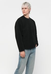 Svart sweatshirt med en texturerad design, rund halsringning och långa ärmar, tillsammans med ljusblå jeans.