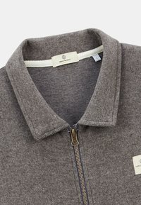 Veste zippée grise en tissu texturé tricoté. Dotée d'un col, d'une fermeture éclair dorée et d'une étiquette à l'intérieur. Taille L.