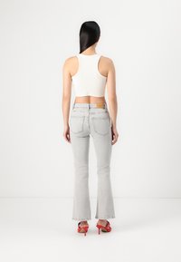 Top court blanc associé à un jean évasé gris clair. Le jean présente un design classique à cinq poches et une patch en cuir beige à l'arrière.
