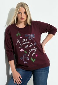 Bordowy sweatshirt z długimi rękawami, zawierający świąteczny tekst oraz dekoracyjne elementy: zielone liście, różowe gwiazdki i grafikę wstążki.