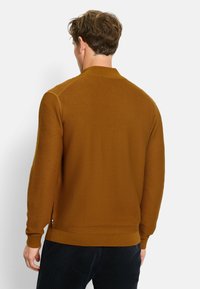 Brauner gerippter Strickpullover mit Kragen, langen Ärmeln und taillierter Säume, von hinten vor einem neutralen Hintergrund getragen.