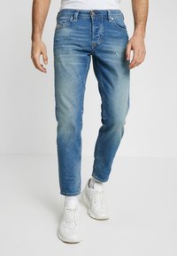 Ljusblå denimjeans med slim fit, blekta detaljer, fem fickor och knappstängning, kombinerat med vita sneakers.