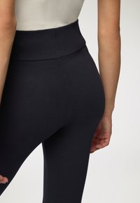 Czarne legginsy z wysokim stanem, wykonane z elastycznej tkaniny, o gładkiej fakturze i dopasowanym kroju, z eleganckim designem i bez widocznych wzorów.