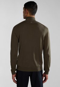 Suéter verde oliva con cuello alto, puños acanalados y dobladillo. Presenta un pequeño acento en rojo, blanco y azul en la nuca de la parte trasera.