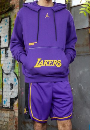 Sudadera morada con detalles amarillos y el logo de los Lakers, que cuenta con un bolsillo frontal y cremalleras. Combinada con pantalones cortos morados a juego.