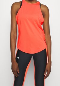 Canotta atletica arancione brillante con orlo curvo, spalline nere, indossata con leggins neri con pannelli laterali arancioni e logo.