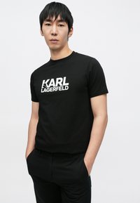 Fekete pamut póló fehér "KARL LAGERFELD" logóval. Rövid ujjú, kerek nyakú, laza szabású, nincs rajta további minta vagy díszítés.