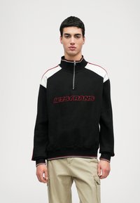 Μαύρο φούτερ με φερμουάρ και λευκές λεπτομέρειες στους ώμους, κόκκινες ραφές και κεντημένο κείμενο "LETS FRANS" στο μπροστινό μέρος, με χαλαρή εφαρμογή.