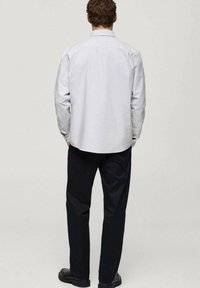 Cămașă lungă gri deschis cu guler tip button-down, asociată cu pantaloni închiși la culoare. Textură netedă, croială lejeră și design minimalist.