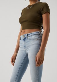 Olivgrön, ribbad crop top som matchas med ljusblå skinny jeans med knapplist och subtila blekningar. Silverkedja synlig.