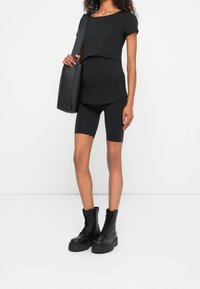 Svart kortärmad topp, åtsittande runt midjan, parat med svarta cykelbyxor och kraftiga svarta snörkängor. Svart väska med bred rem.