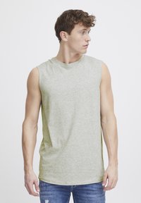Mouwloze lichtgroene t-shirt van zachte stof, met een ronde halslijn en een relaxte pasvorm, gecombineerd met blauwe versleten spijkerbroek.