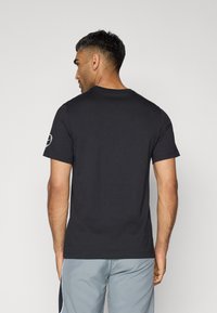 Sort bomulds t-shirt med rund hals og korte ærmer. Har et logo på venstre ærme. Glat tekstur, tætsiddende design.