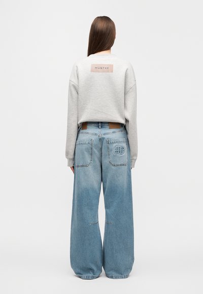 Γκρι φούτερ με ορθογώνιο λογότυπο, σε συνδυασμό με ανοιχτό μπλε τζιν παντελόνι φαρδιάς γραμμής με πίσω τσέπες και ραφές λεπτομέρειες.