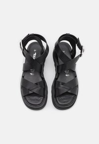 Paire de sandales en cuir noir avec lanières croisées et boucles argentées, taille 37, sur fond blanc.