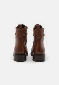 Stivaletti in pelle marrone con una texture liscia, cerniere laterali e cinturini decorativi, dotati di una suola spessa per maggiore stabilità.