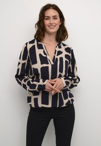 Lange mouwen, V-hals blouse in beige met een marineblauw abstract geometrisch patroon. Kenmerkt zich doorGathered mouwen en knoopmanschetten.