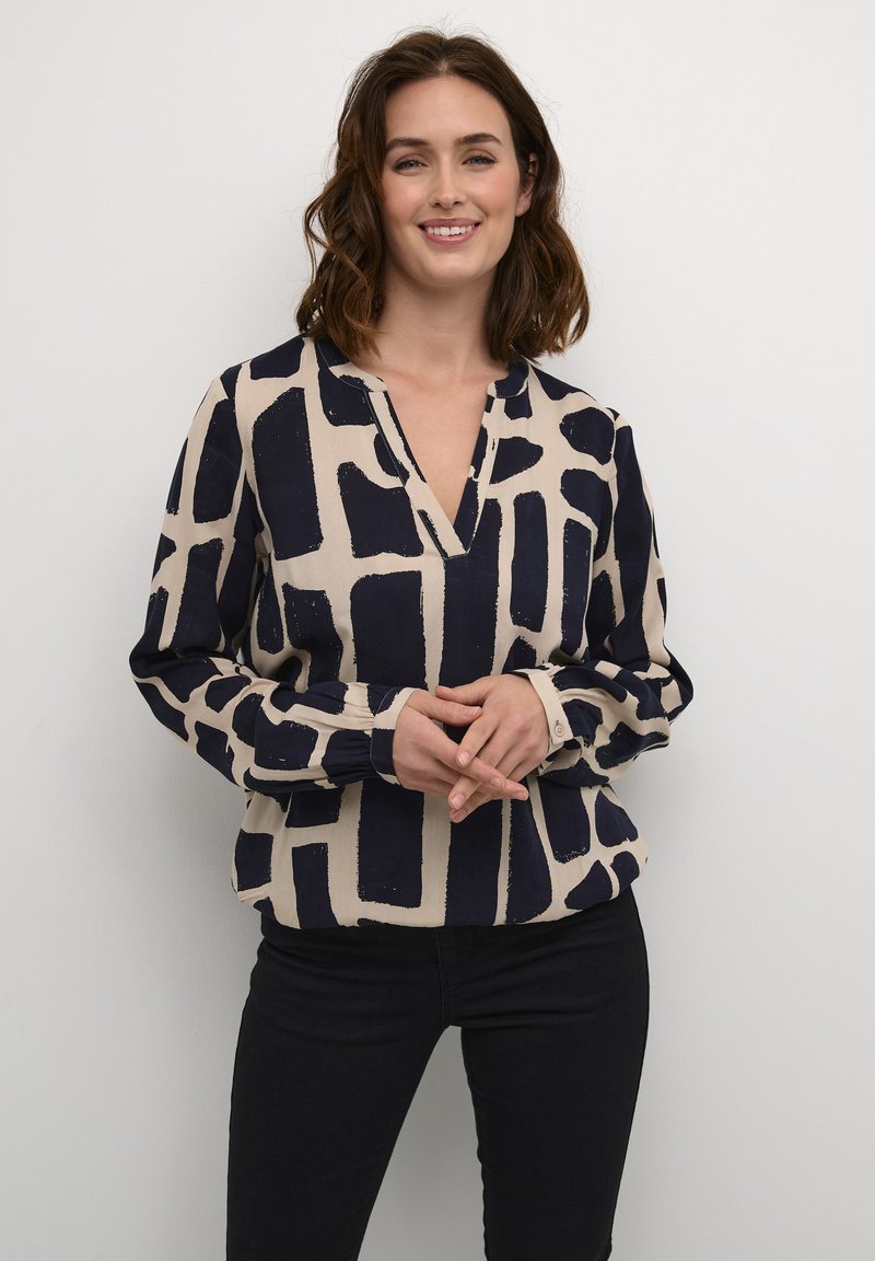 Lange mouwen, V-hals blouse in beige met een marineblauw abstract geometrisch patroon. Kenmerkt zich doorGathered mouwen en knoopmanschetten.