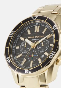 Orologio in metallo dorato con cassa rotonda con lunetta nera, quadrante nero testurizzato, indici delle ore dorati e tre sottodial. Resistentesi all'acqua fino a 100 metri.