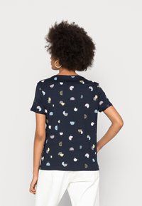 Camiseta de color azul marino con mangas cortas, que presenta patrones abstractos multicolores. Confeccionada en tejido suave, tiene un corte relajado y un escote redondo.