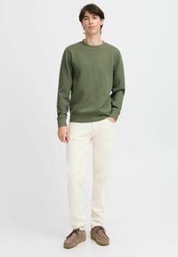 Sudadera verde de cuello redondo con puños acanalados, combinada con pantalones beige claros y zapatos de ante marrón. Diseño simple y casual.