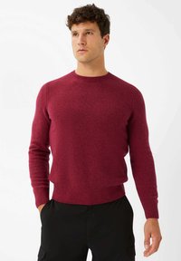 Burgunderfarbener Pullover aus strukturiertem Strickstoff, mit rundem Halsausschnitt und langen Ärmeln, kombiniert mit schwarzen Hosen.