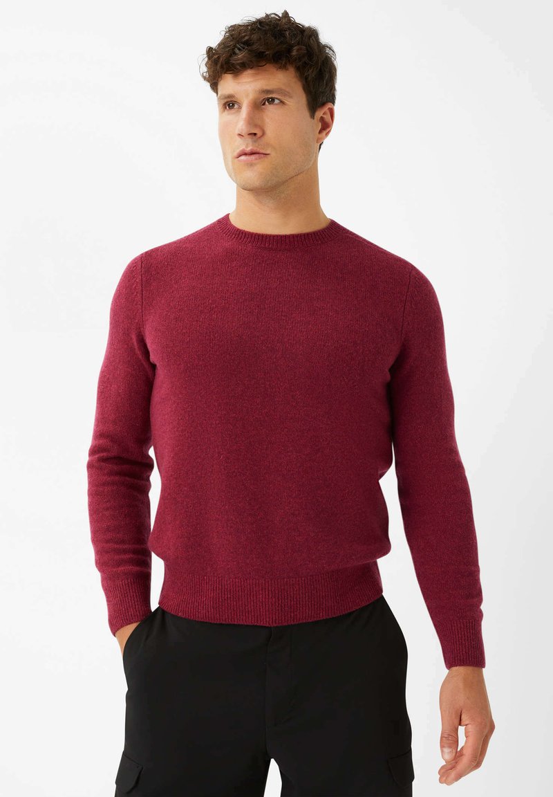 Burgunderfarbener Pullover aus strukturiertem Strickstoff, mit rundem Halsausschnitt und langen Ärmeln, kombiniert mit schwarzen Hosen.