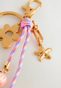 Llaveros de metal dorado con forma de flor, que presentan cordones trenzados en tonos púrpura, rosa y naranja, además de un encantador estrella de mar dorado.