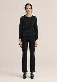 Svart stickad cardigan med rund halsringning och knäppning, i kombination med svarta åtsittande byxor och ankelboots. Enkel, strömlinjeformad design.